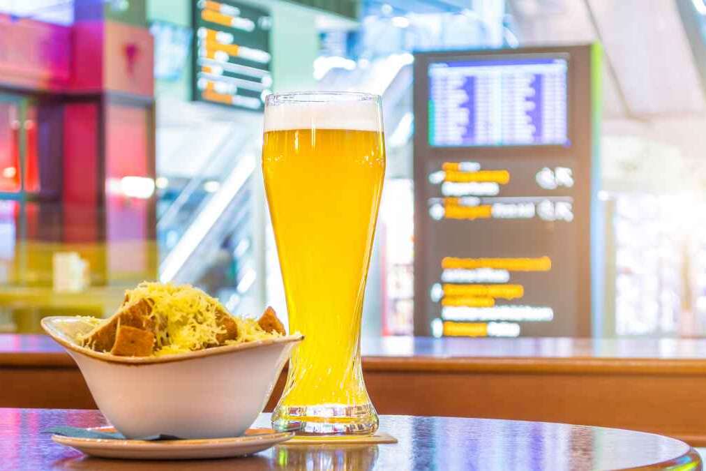 A glass of beer and a plate of breadcrumbs and cheese. In the background, online board displays flights to the airport. Concept expecting a voyage trip in a cafe, bar, retsorane drinking drinks
