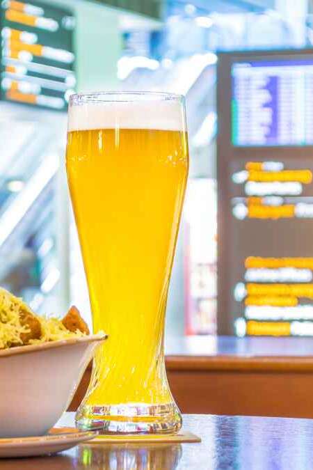 A glass of beer and a plate of breadcrumbs and cheese. In the background, online board displays flights to the airport. Concept expecting a voyage trip in a cafe, bar, retsorane drinking drinks