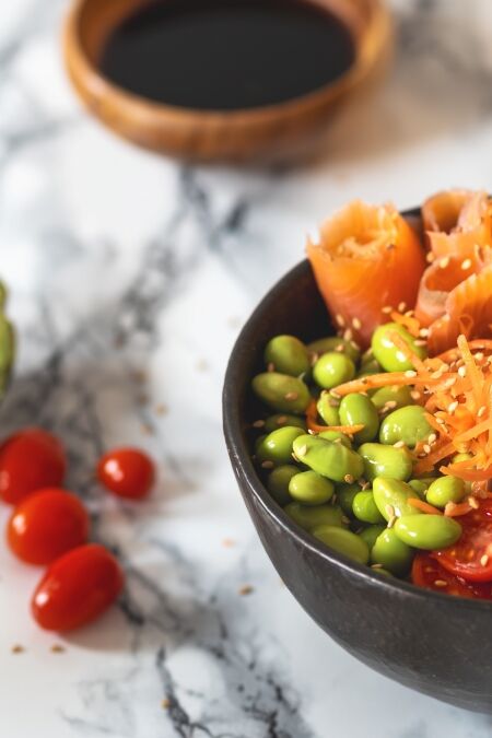 Nutritious poke bowl with avocado, edamame, cherry tomatoes, shredded carrots, shrimps and salmon on a marble background. Healthy food concept