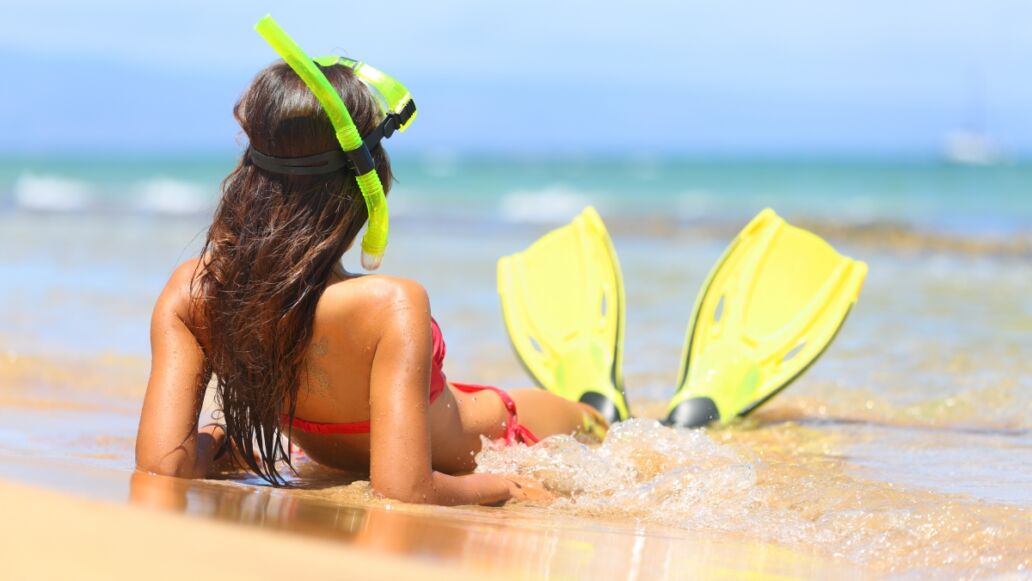 Woman relaxing on summer beach vacation holidays lying in sand with snorkeling mask and fins smiling happy enjoying the sun on sunny summer day on Maui, Hawaii, USA.