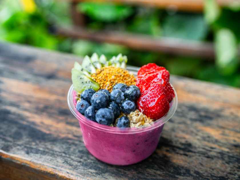 Acai bowl healthy breakfast in to go plastic takeout bowl frozen yogurt smoothie with fresh fruits, berries, blueberries at Hawaii cafe. Foodie food snack.