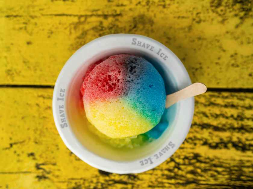 Shave Ice Hawaii local food hawaiian snow cone with three colors colored dyes. Frozen dessert food top view of bowl on retro yellow table.