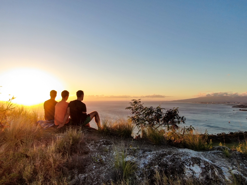 Aerial drone view of three young male hikers enjoying the sunset view on the summit of Diamond Head Crater, a famous tourist destination in Honolulu, Oahu.Hawaii, USA.