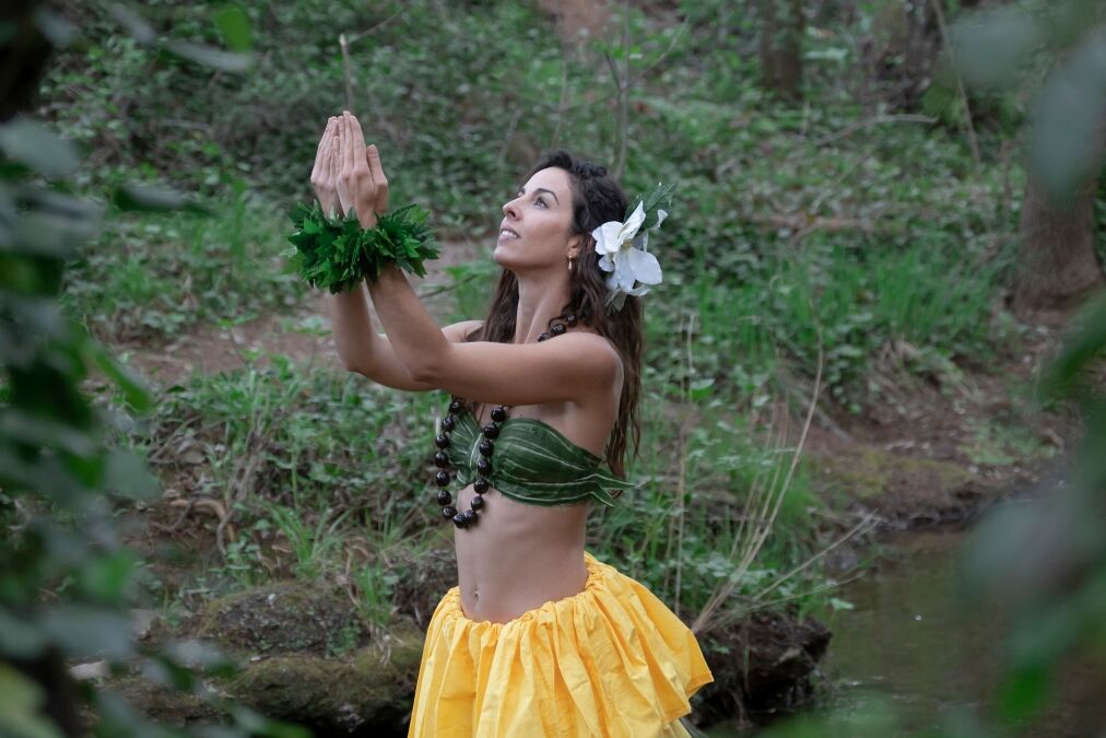 A young woman is looking at the sky with her hands together performing a typical Hawaiian dance connecting with nature.