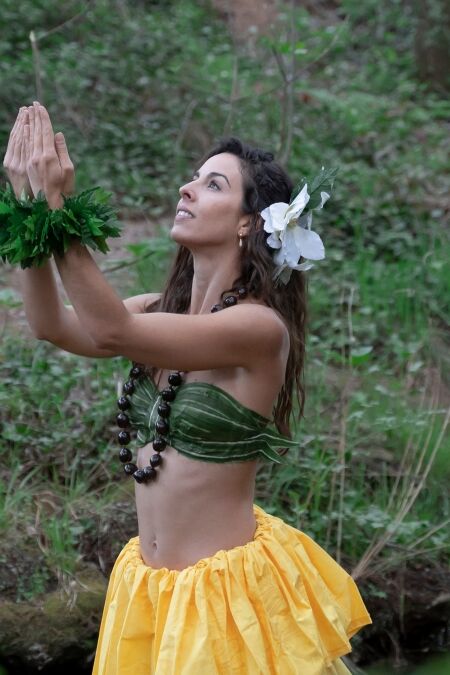 A young woman is looking at the sky with her hands together performing a typical Hawaiian dance connecting with nature.
