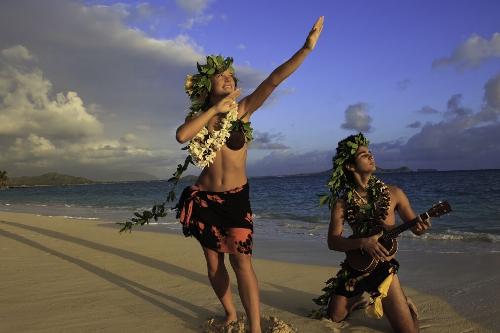 couple dancing hula on the beach at sunrise with the man playing ukulele