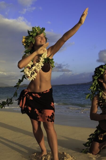 couple dancing hula on the beach at sunrise with the man playing ukulele