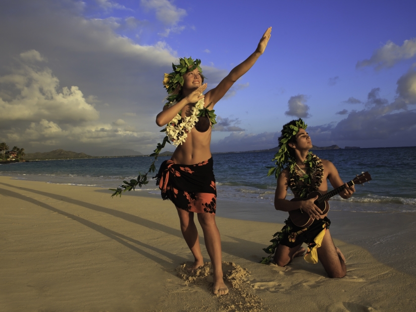 couple dancing hula on the beach at sunrise with the man playing ukulele