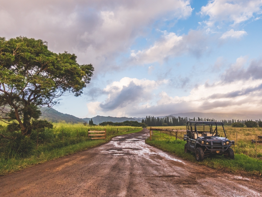 scenic view of tropical landscape with clouds and sky just after the rain. Dirt road with all terrain vehicle parked along side.