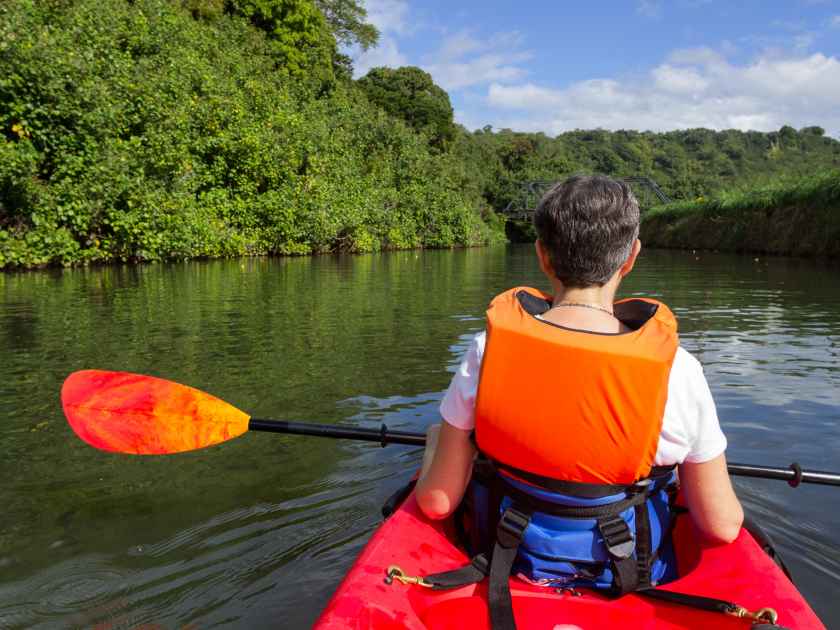 Retired caucasian lady in a red canoe or sea kayak on Hanalei river approaching the old steel bridge in Kauai