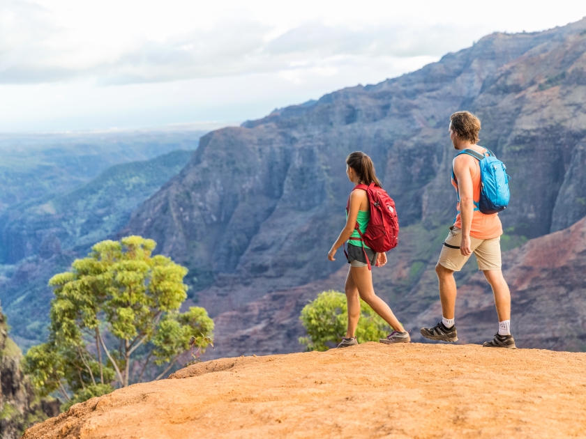 Hikers couple hiking in mountains landscape. Woman and man walking on hike in Waimea Canyon State Park, Kauai, Hawaii, USA. Looking at view happy enjoying healthy outdoor lifestyle.