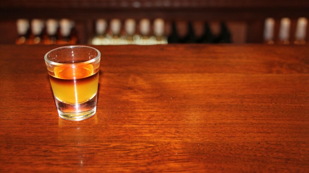 Koloa Rum on Kauaii, Hawaii - detail on the shot with dark coffee rum on the wooden table with blurred bottles in the background.