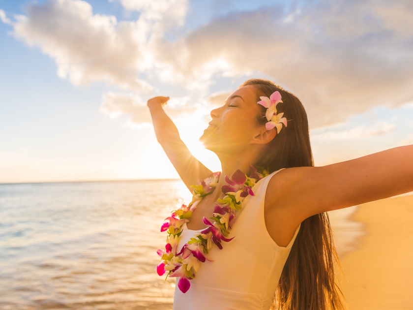 Hawaii hula luau woman wearing hawaiian lei flower necklace on Waikiki beach dancing with open arms free on hawaiian vacation. Asian girl with fresh flowers hair, traditional polynesian dance.