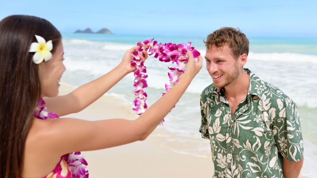 Hawaii woman giving lei garland of pink orchids welcoming tourist on Hawaiian beach. Portrait of a Polynesian culture tradition of giving a flower necklace to a guest as a welcome gesture.