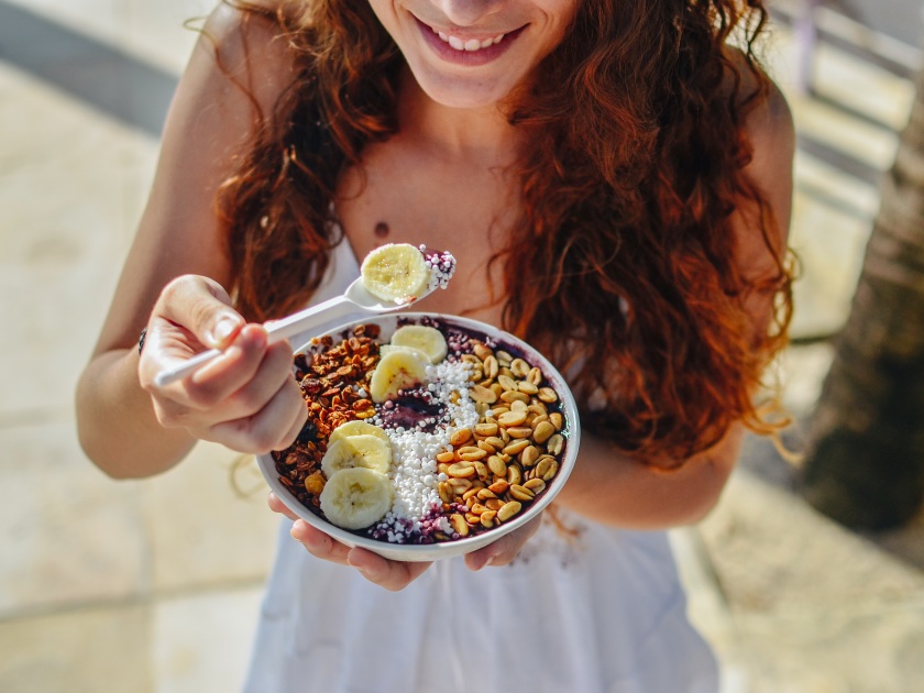 Acai bowl woman eating morning breakfast at cafe. Closeup of fruit smoothie healthy diet for weight loss with berries and oatmeal. Organic raw vegan healthy food.