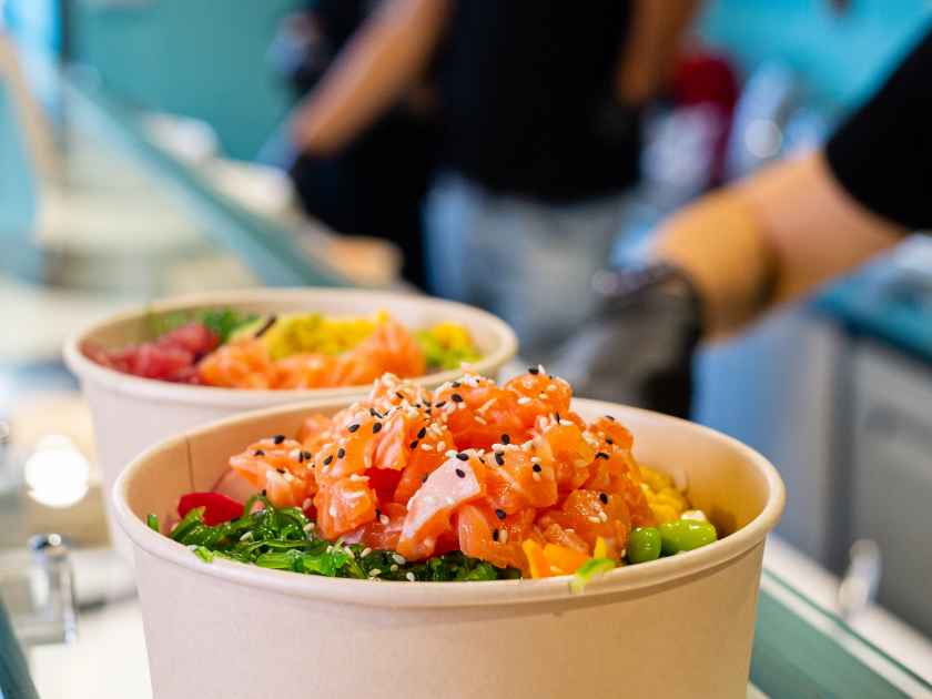 Food delivery of traditional Hawaiian cuisine. Packaging cooked poke bowls into paper bag, wearing protective gloves. Healthy vegetarian eating. Asian vegan raw meal.
