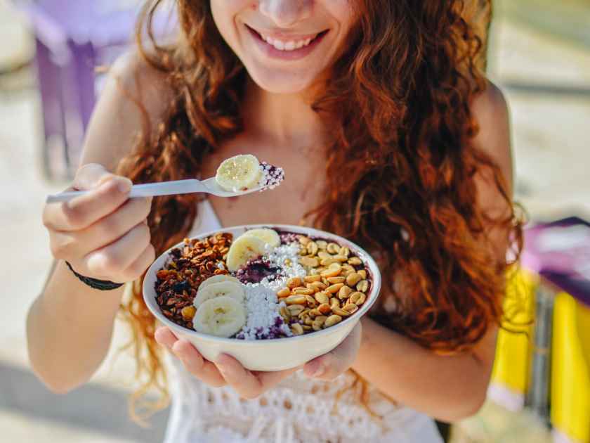 Acai bowl woman eating morning breakfast at cafe. Closeup of fruit smoothie healthy diet for weight loss with berries and oatmeal. Organic raw vegan healthy food.