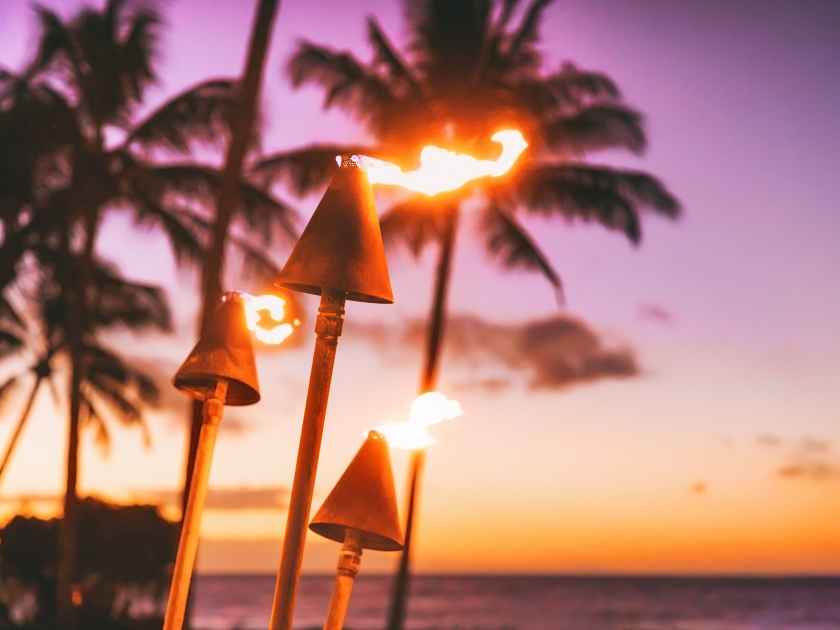 Hawaii luau beach party at sunset. Hawaiian tiki torches lighted up with fire at luxury resort hotel restaurant. Panoramic banner of hawaiian aloha spirit.