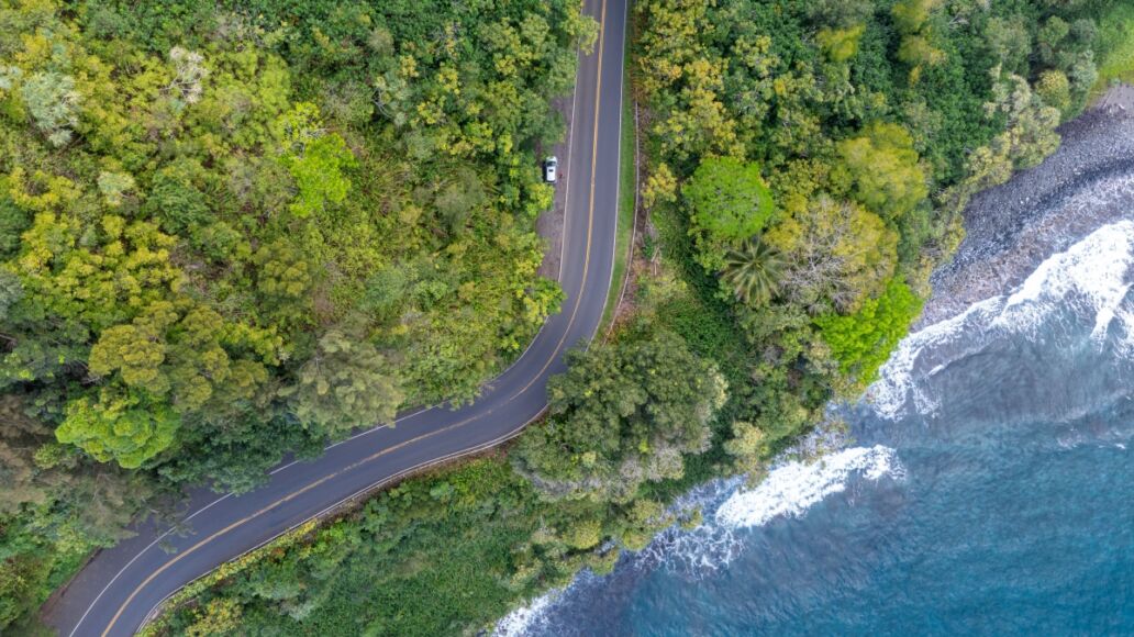 An aerial view of a winding road along a lush tropical coastline with crystal clear turquoise water. Road to Hana, Maui Hawaii.