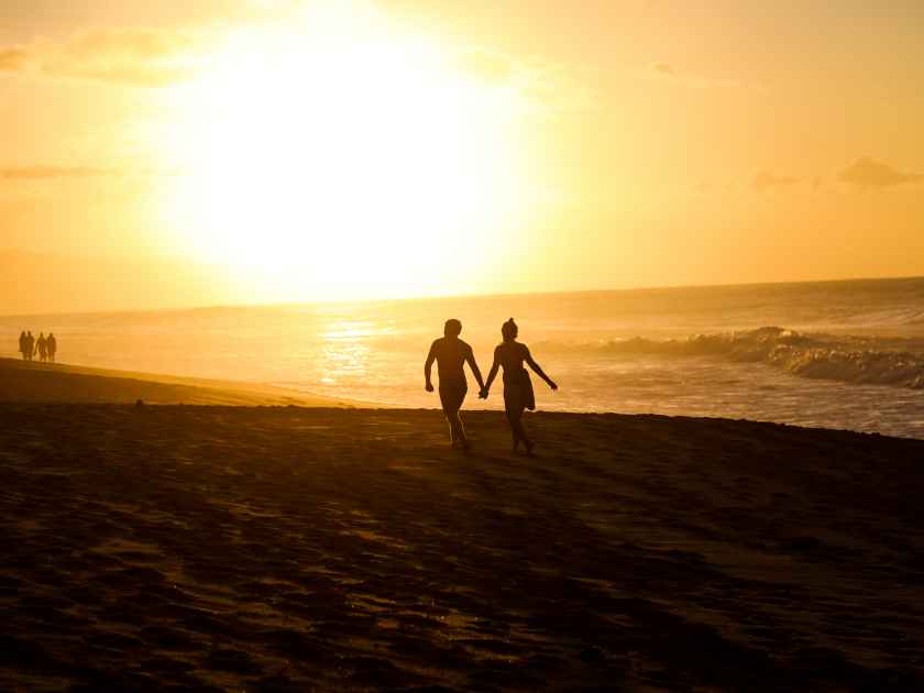 Romantic Couple Holds Hands While Walking on Beach in Oahu Hawaii near Banzai Pipeline at Sunset