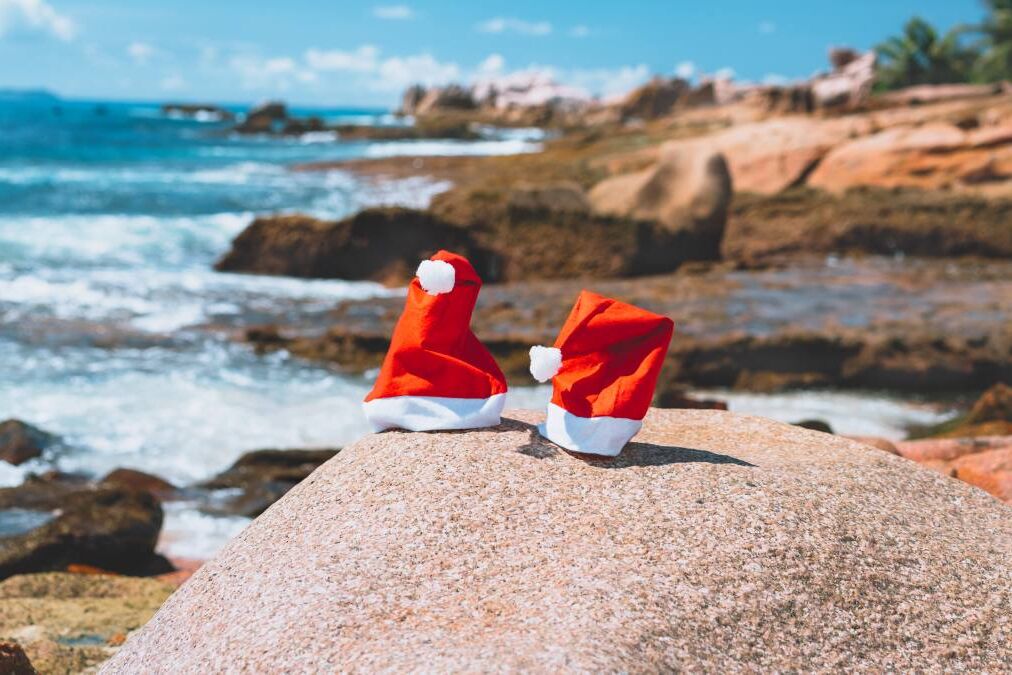 Couple of santa claus hat on tropical exotic paradise sandy beach with ocean waves and rocky coastline in background