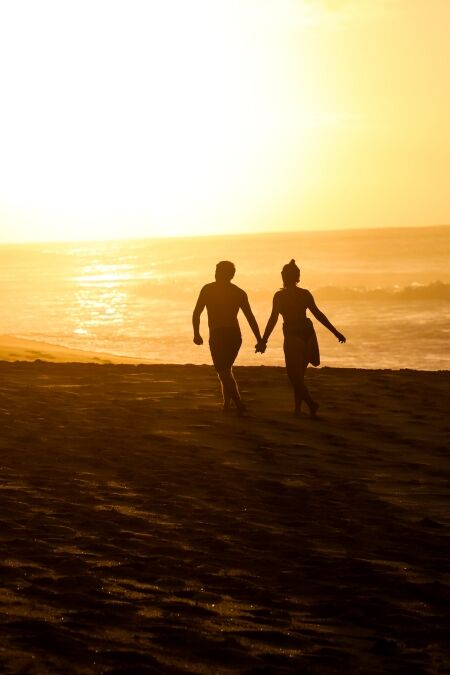 Romantic Couple Holds Hands While Walking on Beach in Oahu Hawaii near Banzai Pipeline at Sunset