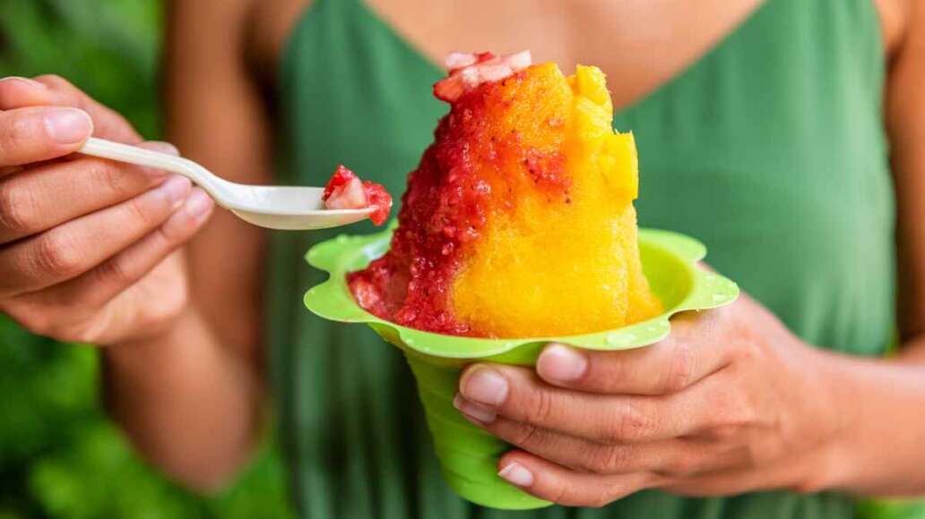 Shave Ice Hawaii local food woman eating hawaiian shaved ice cream treat in Honolulu Waikiki beach, Hawaii , USA.