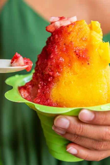 Shave Ice Hawaii local food woman eating hawaiian shaved ice cream treat in Honolulu Waikiki beach, Hawaii , USA.