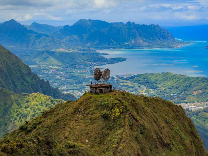 Aerial view of CCL Building bunker at the top of Stairway to Heaven or Haiku Stairs with mountains, coastline and Chinaman's Hat island in the background in Honolulu, Hawaii viewed from a helicopter