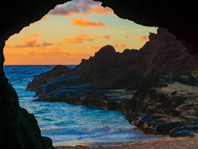 The view from a cave at Halona Cove, Oahu, Hawaii includes waves crashing the beach and a rocky ledge