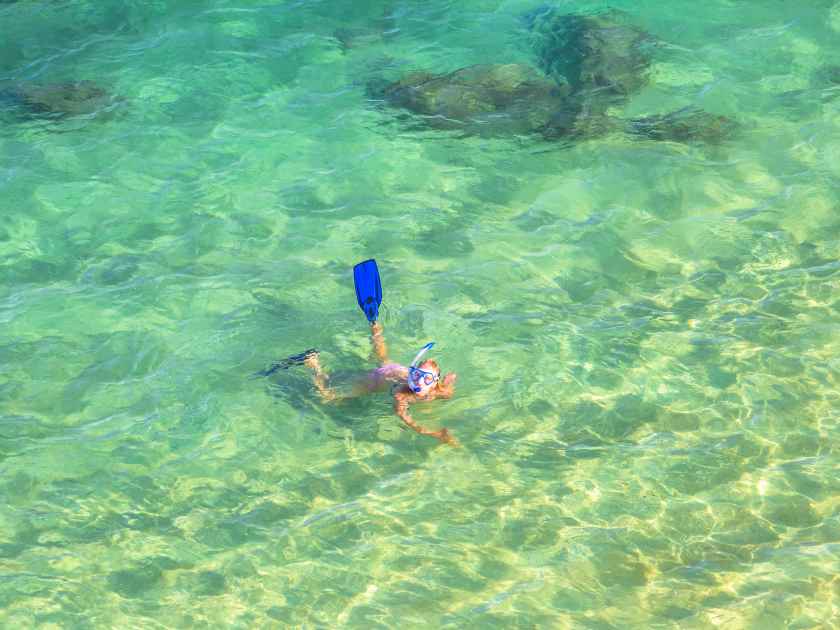 Beautiful smiling woman snorkeling over coral reef in Hanauma Bay Nature Preserve, Oahu, Hawaii, USA. Female snorkeler swims in tropical sea with american flag bikini. Watersport activity in Hawaii.