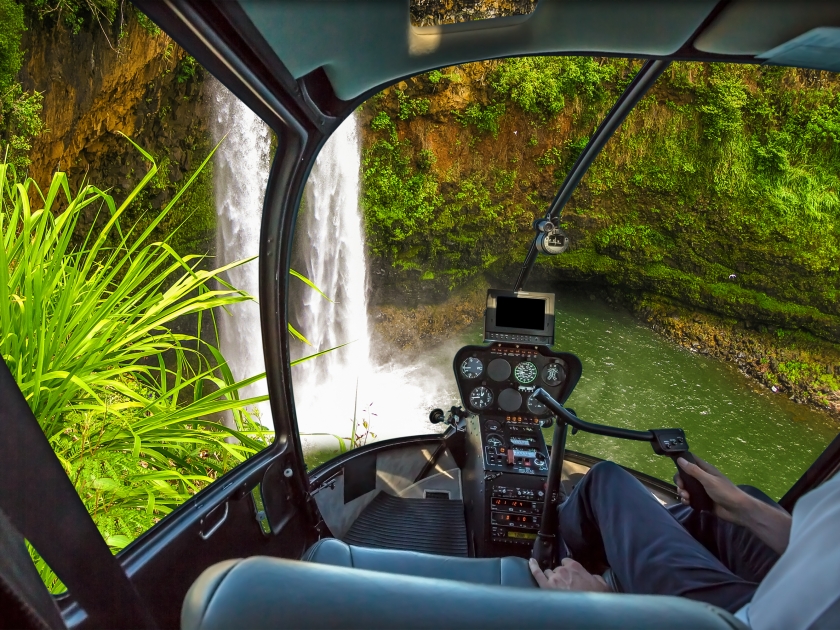 Helicopter cockpit flies in ropical Manawaiopuna Falls also called Jurassic Park Falls, Kauai, Hawaii, United States, with pilot arm and control board inside the cabin.