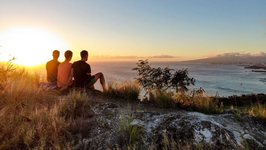 Aerial drone view of three young male hikers enjoying the sunset view on the summit of Diamond Head Crater, a famous tourist destination in Honolulu, Oahu.Hawaii, USA.