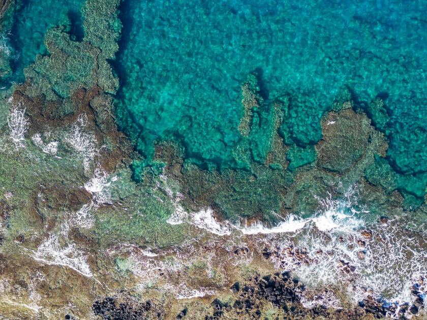 A top down aerial photo of the blue waters of Hawaii and coral reefs off of the Big Island. With beautiful blue colors and texture of the reefs.