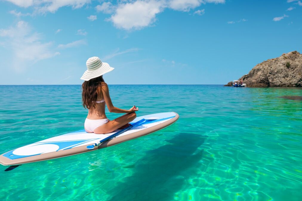 A beautiful young woman relaxes on a SUP board in the sea near the island. Standup paddleboarding on Hawaii.