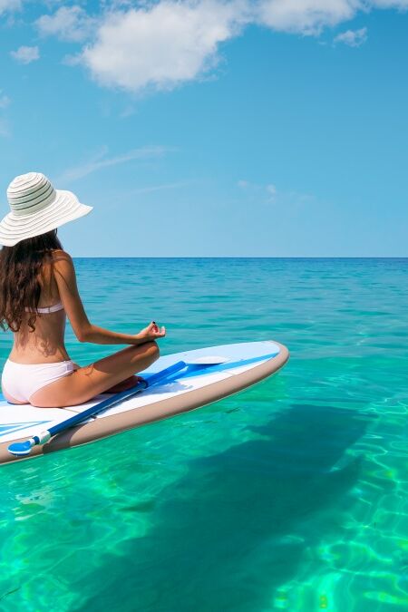 A beautiful young woman relaxes on a SUP board in the sea near the island. Standup paddleboarding on Hawaii.
