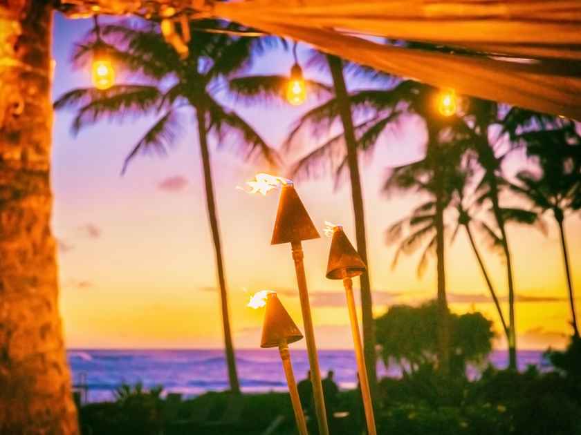 Hawaii luau party with fire torches at sunset. Hawaiian icon, lights burning at dusk at Waikiki beach resort restaurant for outdoor lighting cozy atmosphere.