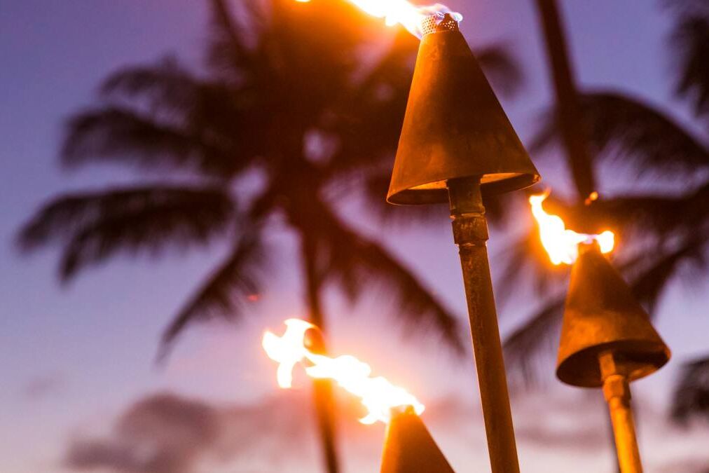 Hawaii sunset with lit tiki torches. Hawaiian icon, lights burning at dusk at beach resort or restaurants for outdoor lighting and decoration, cozy atmosphere.