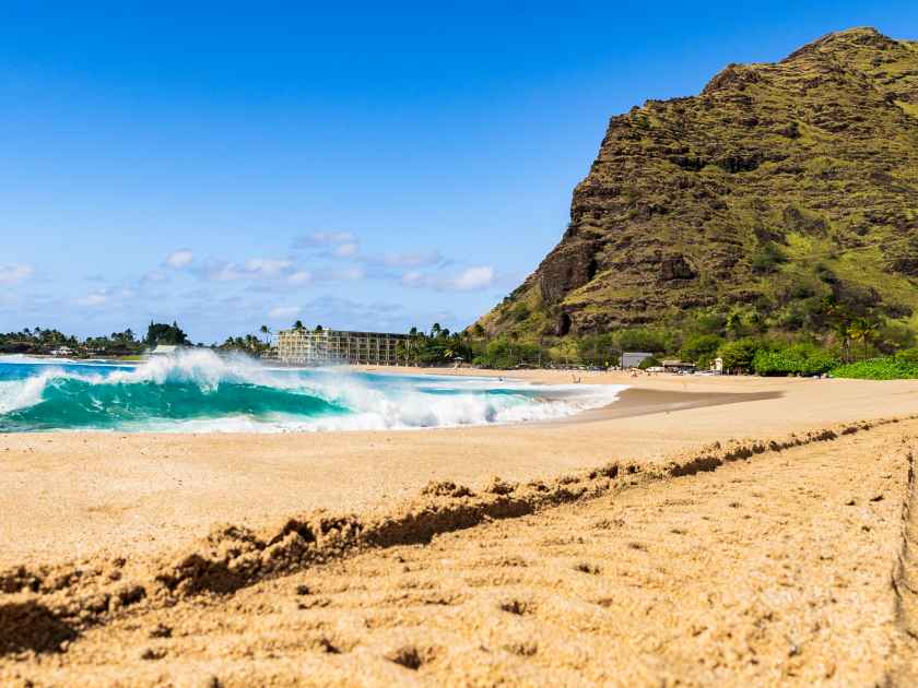 Sunny day at Makaha beach on the west side of the island of Oahu in Hawaii amidst beautiful green mountains with volcanic formation in front of the blue sea