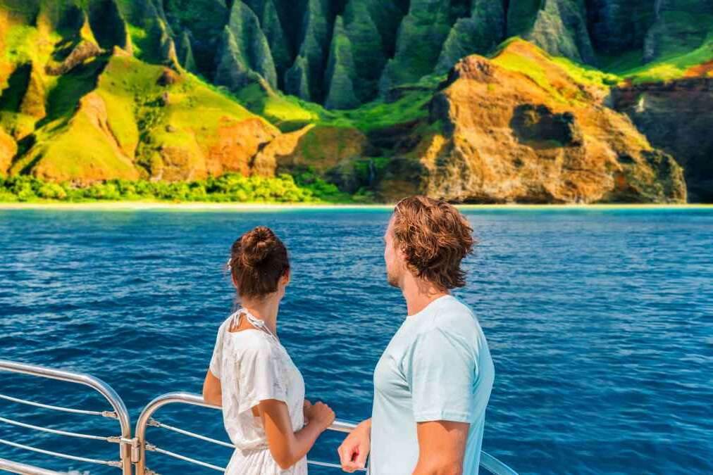 Hawaii Kauai Na Pali coast landscape scenic cruise. Couple watching dramatic mountains famous tourist destination on boat deck. Cruise ship on summer travel vacation and woman tourists relaxing.