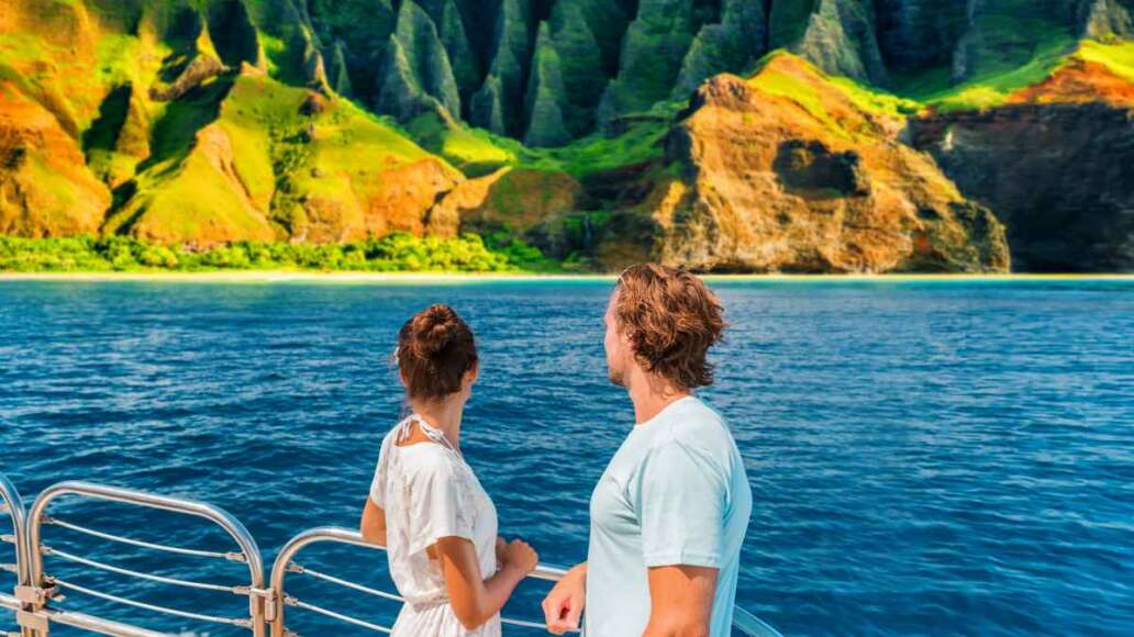 Hawaii Kauai Na Pali coast landscape scenic cruise. Couple watching dramatic mountains famous tourist destination on boat deck. Cruise ship on summer travel vacation and woman tourists relaxing.