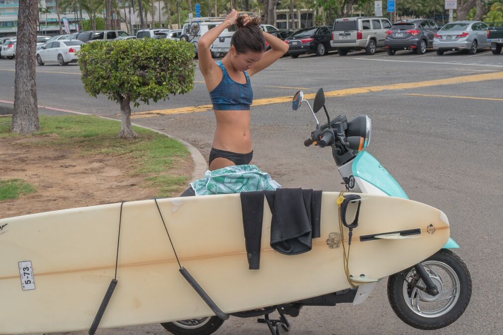 Honolulu, Hawaii, USA, Nov. 28, 2017. Young Hawaiian surfer girl with her surfboard loaded on her scooter for the trip home after a morning of surfing.