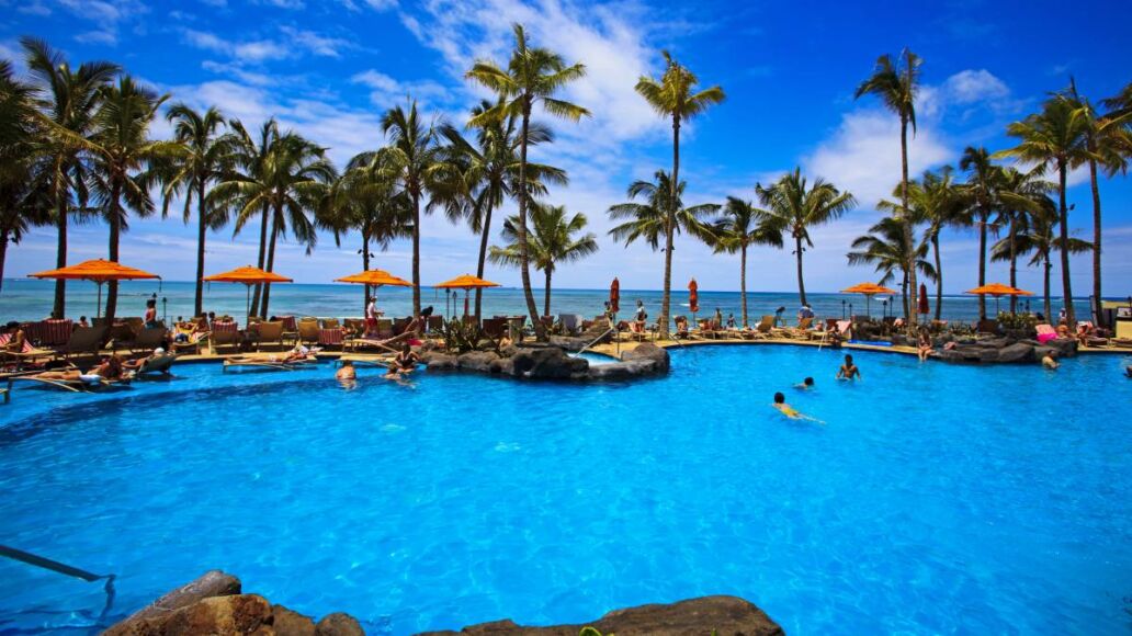 The swimming pool at the Sheraton Waikiki hotel sits at waters edge by the blue Pacific Ocean on Waikiki beach, Hawaii