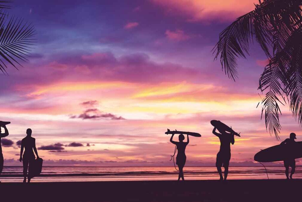 Silhouette of surfer people carrying their surfboards on sunset beach. Panoramic soft style with vintage filter effect for banner background.