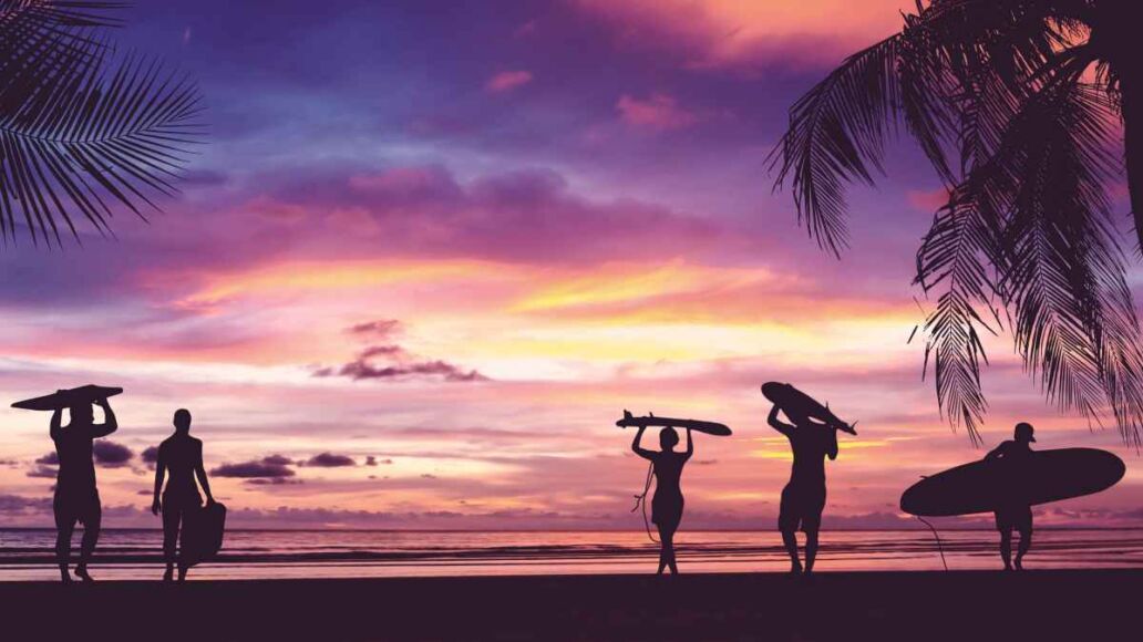 Silhouette of surfer people carrying their surfboards on sunset beach. Panoramic soft style with vintage filter effect for banner background.