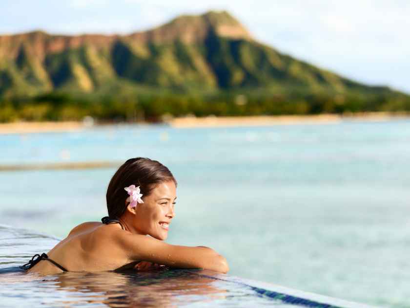Hawaii beach travel vacation woman swimming relaxing at luxury pool hotel resort. Asian young adult on Waikiki beach, Honolulu, Oahu on exotic holidays