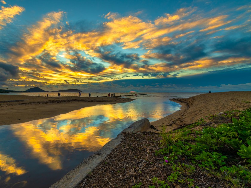 Bright tropical cloud reflections at the Waialae Beach Park in Kahala, Hawaii, at dawn - see the faint red sun rising behind the cloud cover