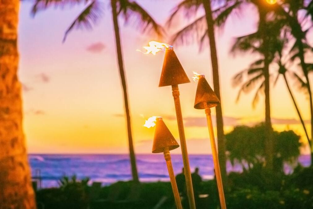 Hawaii luau party with fire torches at sunset. Hawaiian icon, lights burning at dusk at Waikiki beach resort restaurant for outdoor lighting cozy atmosphere.
