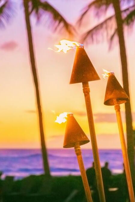 Hawaii luau party with fire torches at sunset. Hawaiian icon, lights burning at dusk at Waikiki beach resort restaurant for outdoor lighting cozy atmosphere.