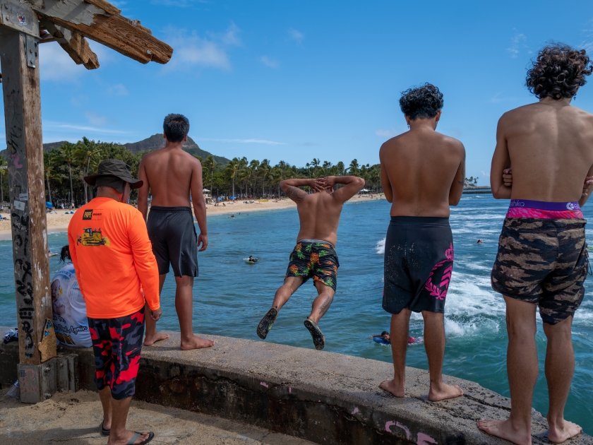 Honolulu, Hawaii, USA. March 14, 2023. Young Hawaiian men jumping from the Waikiki Wall into shallow water.
